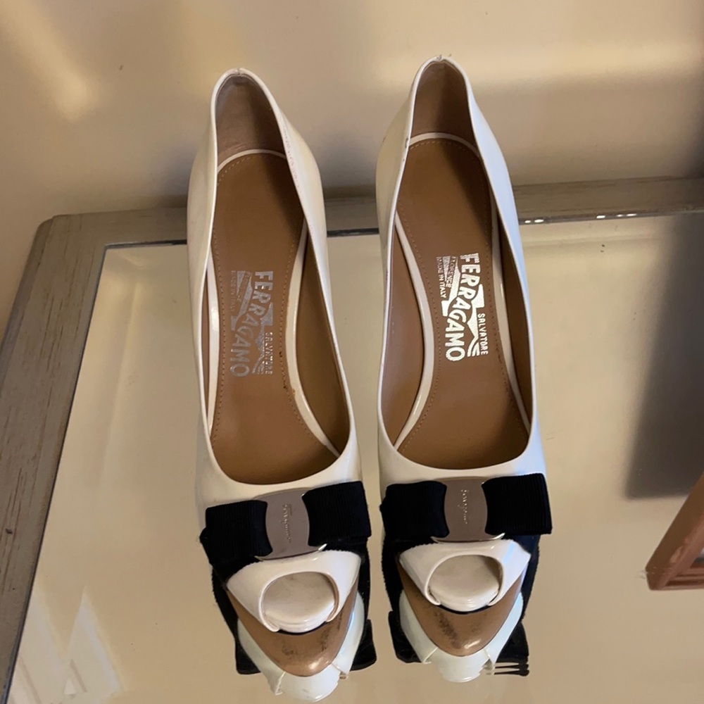 Ferragamo white patent leather pumps with black bow and silver hardware.
